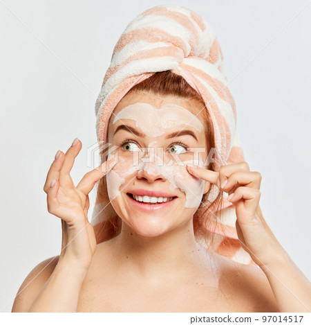 Portrait of young, beautiful, red-haired woman applying face clay mask after shower isolated on white background Portrait of young, beautiful, red-haired woman applying face clay mask after shower isolated on white background 97014517