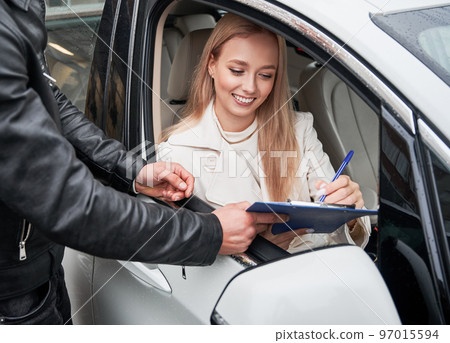 Close up view of young beautiful happy woman customer signing some important documents at new car dealership outdoors, sitting inside new white car Close up view of young beautiful happy woman customer signing some important documents at new car dealership outdoors, sitting inside new white car 97015594
