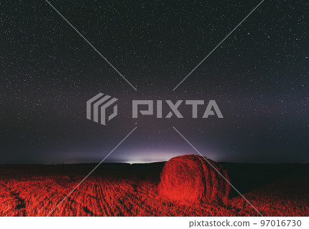 Glowing Stars And Sunset Lights Hay Bales After Harvest. Agricultural Colorful Background Copy Space. Night Starry Sky Above Rural Landscape Field Meadow With Rolls Of Straw In Fields After Harvest 97016730