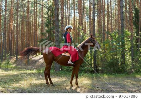 Woman in traditionsl clothes rides a horse in summer forest Woman in traditionsl clothes rides a horse in summer forest 97017896