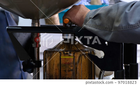 Change engine oil. The male hands of a mechanic drain the old oil from the car into a special container. Old dirty oil being drained from underneath a car during an oil change 97018823
