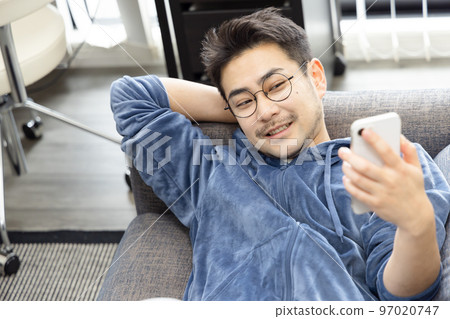 男人在沙發上睡覺時使用智能手機 男人在沙發上睡覺時使用智能手機 97020747