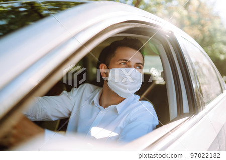 Man driving a car wearing on a medical mask during an epidemic, a driver- taxi in a mask. Covid-2019 Man driving a car wearing on a medical mask during an epidemic, a driver- taxi in a mask. Covid-2019 97022182