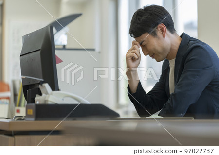 A businessman in his thirties holding his head at his desk A businessman in his thirties holding his head at his desk 97022737