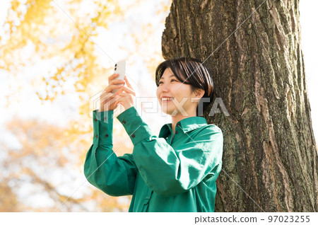 一個女人靠在一棵樹上操作智能手機 97023255