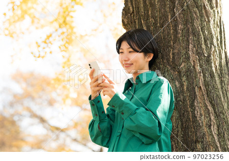 A woman leaning against a tree and operating a smartphone A woman leaning against a tree and operating a smartphone 97023256