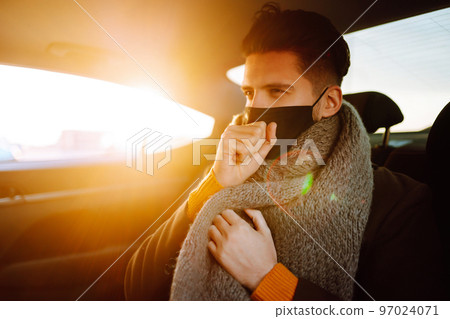 Young man in protective sterile mask in taxi car on a back seat checking her cell phone. Young man in protective sterile mask in taxi car on a back seat checking her cell phone. 97024071