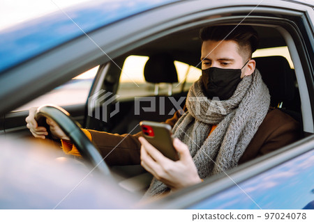 Young man in protective sterile medical mask driving car in quarantine city. Covid -19. Young man in protective sterile medical mask driving car in quarantine city. Covid -19. 97024078