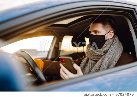 Young man in protective sterile medical mask driving car in quarantine city. Covid -19. Young man in protective sterile medical mask driving car in quarantine city. Covid -19. 97024079