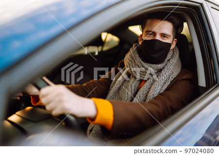 Young man in protective sterile medical mask driving car in quarantine city. Covid -19. Young man in protective sterile medical mask driving car in quarantine city. Covid -19. 97024080