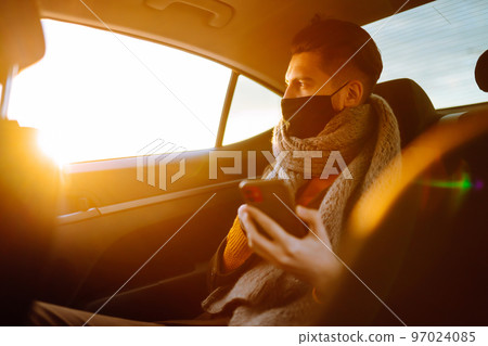 Young man in protective sterile mask in taxi car on a back seat checking her cell phone. 97024085