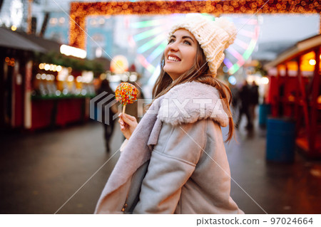 Young woman with caramel apple on Christmas market. Smiling woman in winter style clothes posing. 97024664