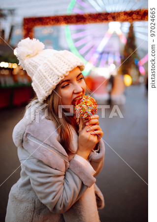 Young woman with caramel apple on Christmas market. Smiling woman in winter style clothes posing. 97024665