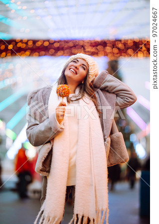 Young woman with caramel apple on Christmas market. Smiling woman in winter style clothes posing. 97024667