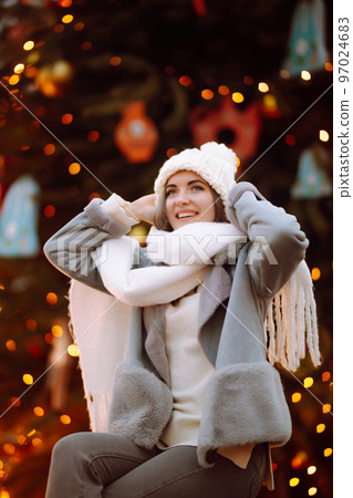 Smiling woman in winter style clothes posing at festive street market. Young woman enjoying winter moments. 97024683