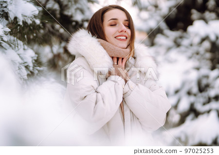 Beautiful woman in winter clothes posing in a snowy park. Young lady walking in a sunny winter day. Beautiful woman in winter clothes posing in a snowy park. Young lady walking in a sunny winter day. 97025253
