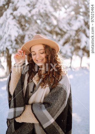 Smiling woman enjoying winter moments in snowy park. Young woman wearing hat, plaid scarf and coat. Smiling woman enjoying winter moments in snowy park. Young woman wearing hat, plaid scarf and coat. 97025464