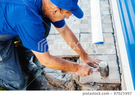 Bricklayer lays tiles. Professional builder in overalls and baseball cap at work. Elderly mason 97025997