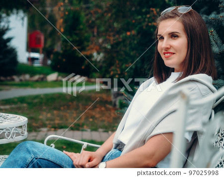 Beautiful Caucasian woman sits on park bench and looks away. Portrait of girl 30 years old.. 97025998