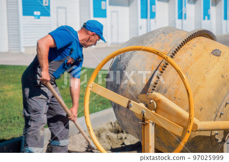 Uniformed construction worker works on construction site on summer day. Elderly bricklayer shovels 97025999