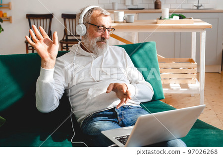 Elderly man making video call on laptop in room waving to screen and chatting with children - modern technologies communication and internet 97026268