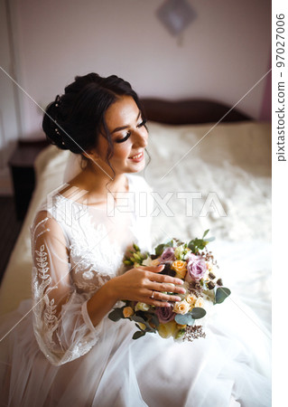 Stylish happy bride is getting ready in the morning. Happy newlywed woman in bedroom. Fashion bride. 97027006