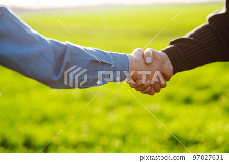 Handshake two farmer on the background of a wheat field at sunset. The concept of the agricultural business. 97027631