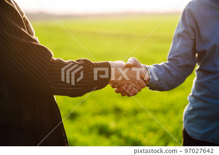 Handshake two farmer on the background of a wheat field at sunset. The concept of the agricultural business. Handshake two farmer on the background of a wheat field at sunset. The concept of the agricultural business. 97027642