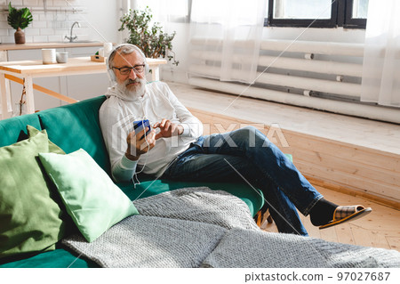 Senior hipster man using phone while listening playlist music on mobile app - Elderly male wearing face protective mask while watching video on smartphone 97027687