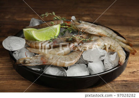 Fresh raw shrimps with lemon slices and ice on wooden table 97028282