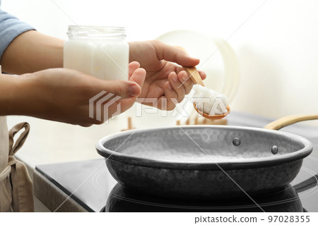 Woman cooking with coconut oil on induction stove, closeup 97028355