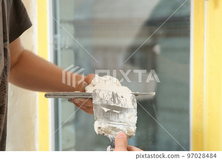 Professional worker with putty knifes and plaster near window indoors, closeup. Interior repair 97028484