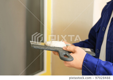Professional worker with putty knifes and plaster near window indoors, closeup. Interior repair Professional worker with putty knifes and plaster near window indoors, closeup. Interior repair 97028488