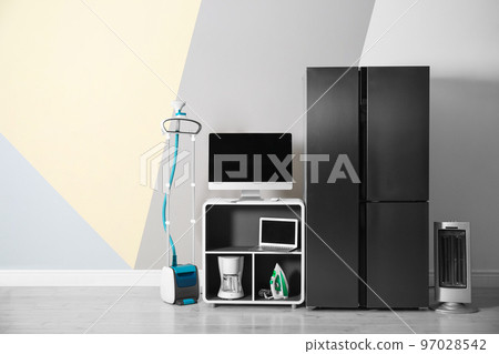 Modern refrigerator and other household appliances near color wall indoors Modern refrigerator and other household appliances near color wall indoors 97028542