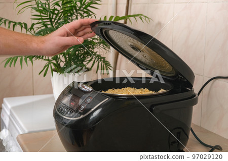 Man closes lid of slow cooker and selects cooking Man closes lid of slow cooker and selects cooking 97029120