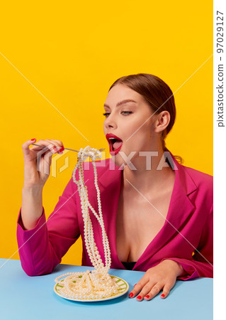 Beautiful young girl in vivid pink jacket eating spaghetti, noodles over yellow background. Delicious Italian food. Food pop art photography. 97029127