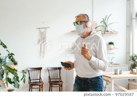 Senior man with medical mask on face dance and using smartphone app for creating playlist music on mobile app copy space - Elderly male having fun dancing with mobile phone technology - Tech and 97029587