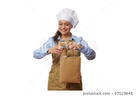 Pretty woman waitress, bartender or confectioner putting a disposable cup of takeaway coffee or tea into a paper eco bag, over white background. Concept of home delivery of hot beverage and fresh food 97029648