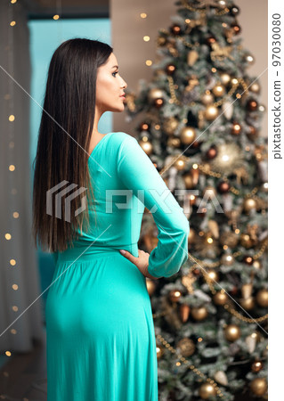 Brunette woman in evening dress near shiny Christmas tree  97030080