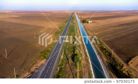 Long asphalt Road with blue water canal, fields aside. Beautiful nature landscape with clear sky. download image 97030173
