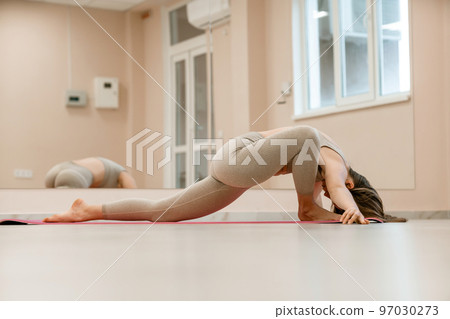 Girl does yoga. Young woman practices asanas on a beige one ton background. 97030273