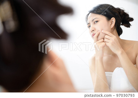 Problem skin. Concerned young asian women popping pimple on cheek while standing near mirror in bathroom. young asian women with acne Problem skin. Concerned young asian women popping pimple on cheek while standing near mirror in bathroom. young asian women with acne 97030793