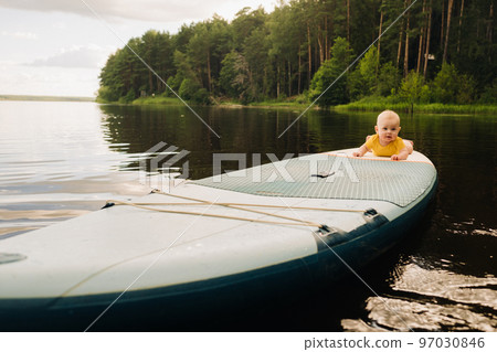 The child lies floating on the water on a large sup board. Water sports 97030846