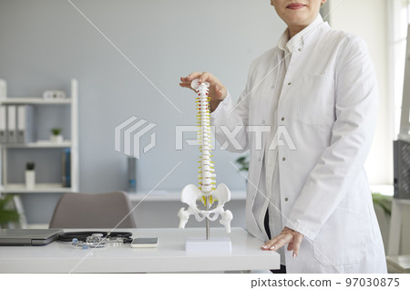 Cropped shot of orthopedic surgeon standing by table with anatomical model of human spine 97030875