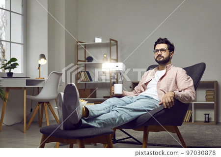Relaxed man sitting in an armchair at home, using a projector, watching a movie, drinking coffee Relaxed man sitting in an armchair at home, using a projector, watching a movie, drinking coffee 97030878