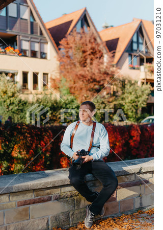 Man Sitting in Old European City And Holding Photo Camera. Contemporary Stylish Blogger And Photographer. Handsome man taking a selfie on a trip in Europe. 97031210