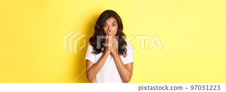 Portrait of startled african-american woman, gasping and covering mouth with hands, looking shocked at camera, standing over yellow background for copy space Portrait of startled african-american woman, gasping and covering mouth with hands, looking shocked at camera, standing over yellow background for copy space 97031223
