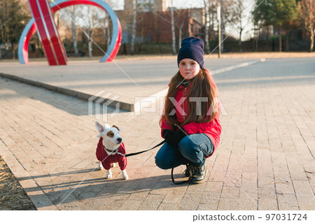 Happy child girl with dog in autumn or winter time. Portrait kid with pet Jack Russell Terrier outdoors - pet owner concept 97031724