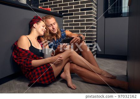 Young couple in love, celebrating a new home in a new apartment, sitting on the kitchen floor, and spending time together having fun. The newlyweds drink wine and have fun Young couple in love, celebrating a new home in a new apartment, sitting on the kitchen floor, and spending time together having fun. The newlyweds drink wine and have fun 97032162