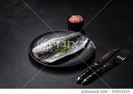 Marinated fillet with spices and herbs of sea herring on a black plate Marinated fillet with spices and herbs of sea herring on a black plate 97033205